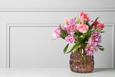 Beautiful bouquet of colorful tulip flowers on white table near light grey wall, space for text