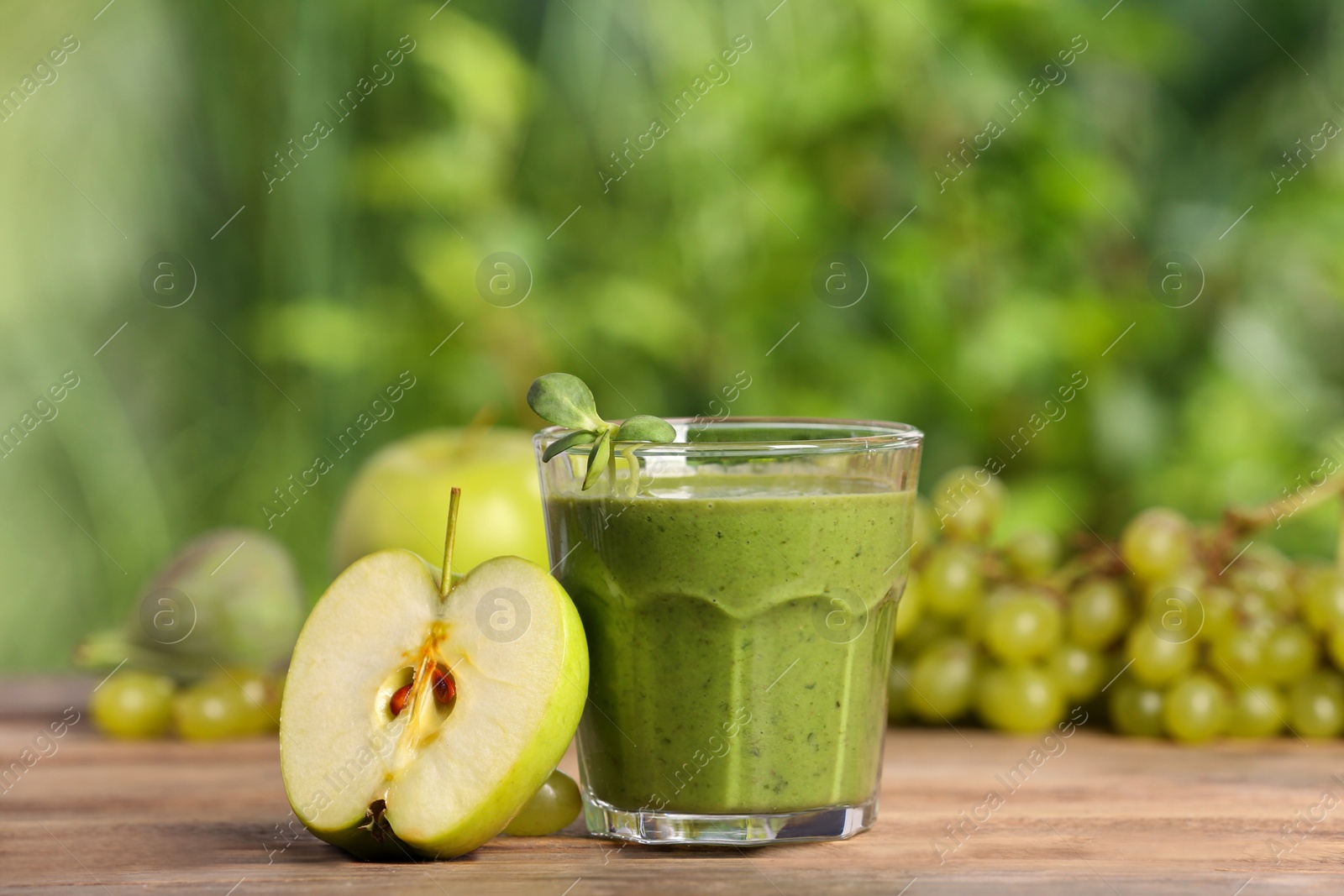 Photo of Glass of fresh green smoothie and ingredients on wooden table outdoors, space for text