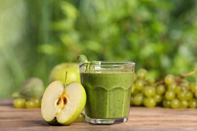 Photo of Glass of fresh green smoothie and ingredients on wooden table outdoors, space for text
