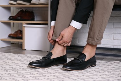 Photo of Man with stylish shoes sitting near shelving unit in hallway, closeup