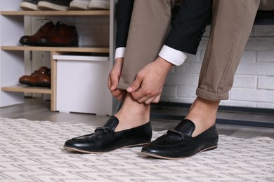 Man with stylish shoes sitting near shelving unit in hallway, closeup