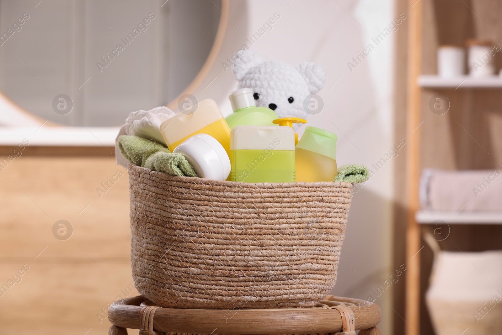 Photo of Wicker basket with baby cosmetic products, bath accessories and toy bear on wooden table indoors