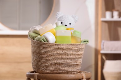 Photo of Wicker basket with baby cosmetic products, bath accessories and toy bear on wooden table indoors