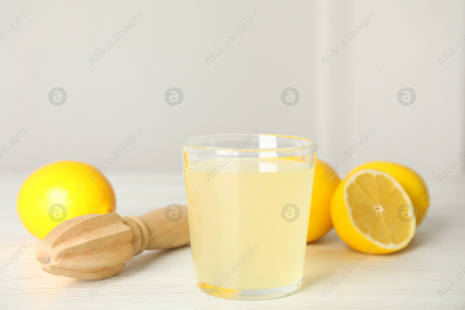 Photo of Freshly squeezed juice, lemons and reamer on white wooden table