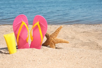 Photo of Stylish flip flops, sun protection cream and starfish on sandy beach, space for text