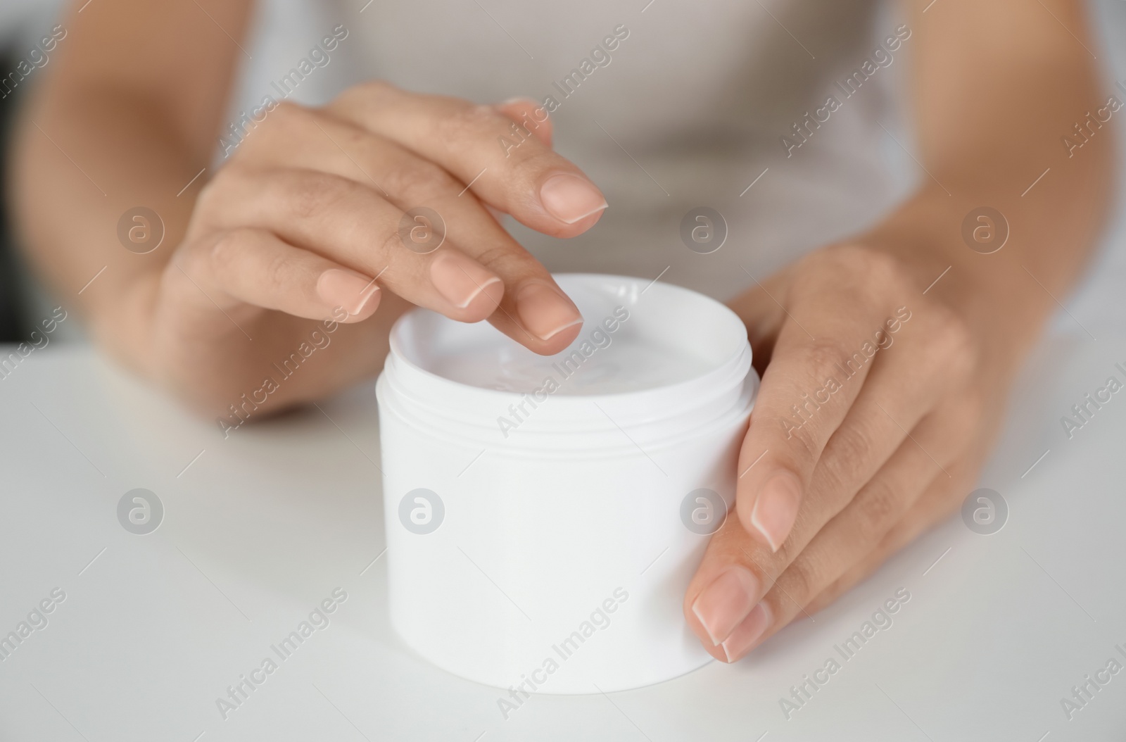 Photo of Woman with jar of moisturizing cream at white table, closeup