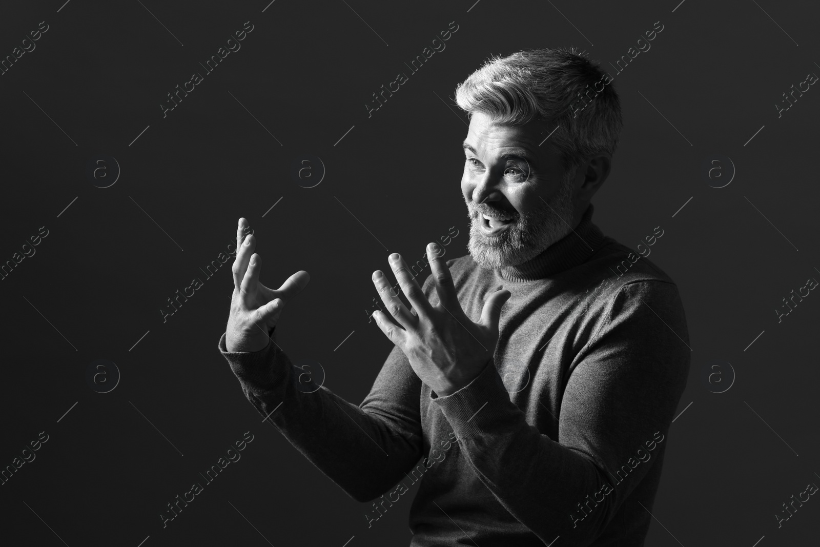 Photo of Portrait of smiling man gesturing on dark background. Black and white effect
