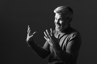 Photo of Portrait of smiling man gesturing on dark background. Black and white effect