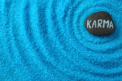 Photo of Stone with word Karma on light blue sea salt, top view. Space for text