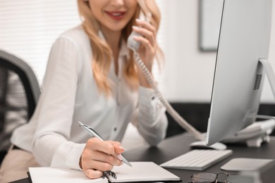 Photo of Secretary talking on phone and taking notes at table in office, closeup