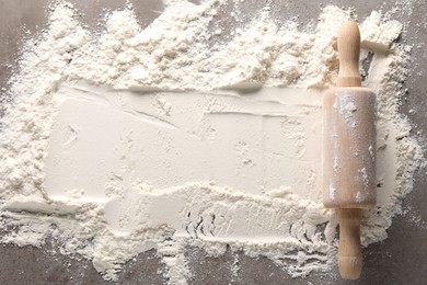 Photo of Scattered flour and rolling pin on grey textured table, top view