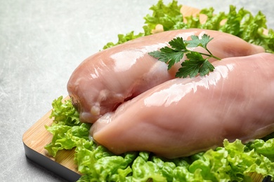 Photo of Wooden board with raw chicken breasts and lettuce on grey background