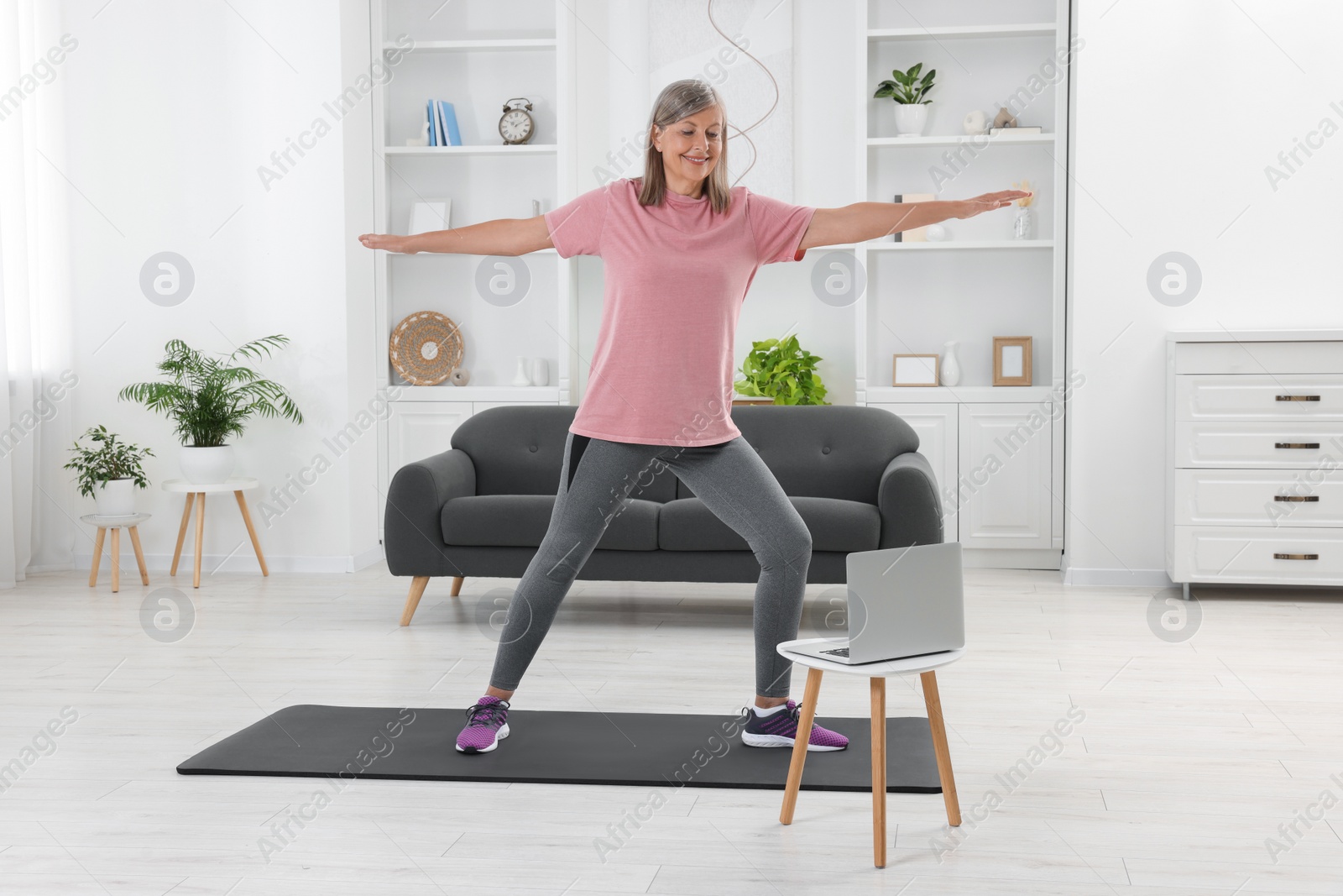 Photo of Senior woman in sportswear doing exercises near laptop at home