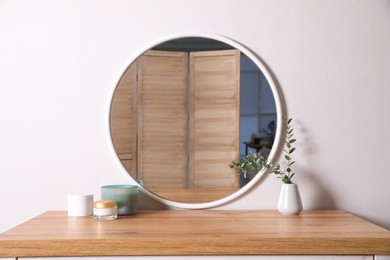 Photo of Trendy round mirror and chest of drawers near white wall. Interior element