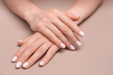 Woman showing her manicured hands with white nail polish on light brown background, closeup