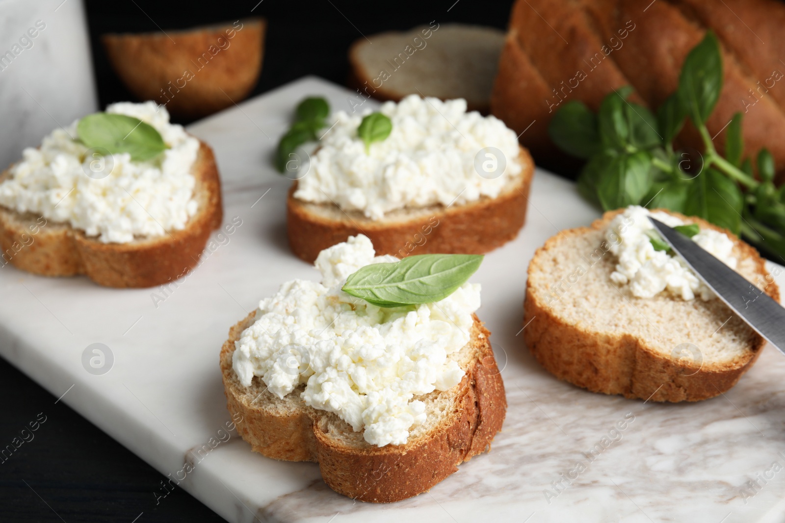 Photo of Bread with cottage cheese and basil on board, closeup