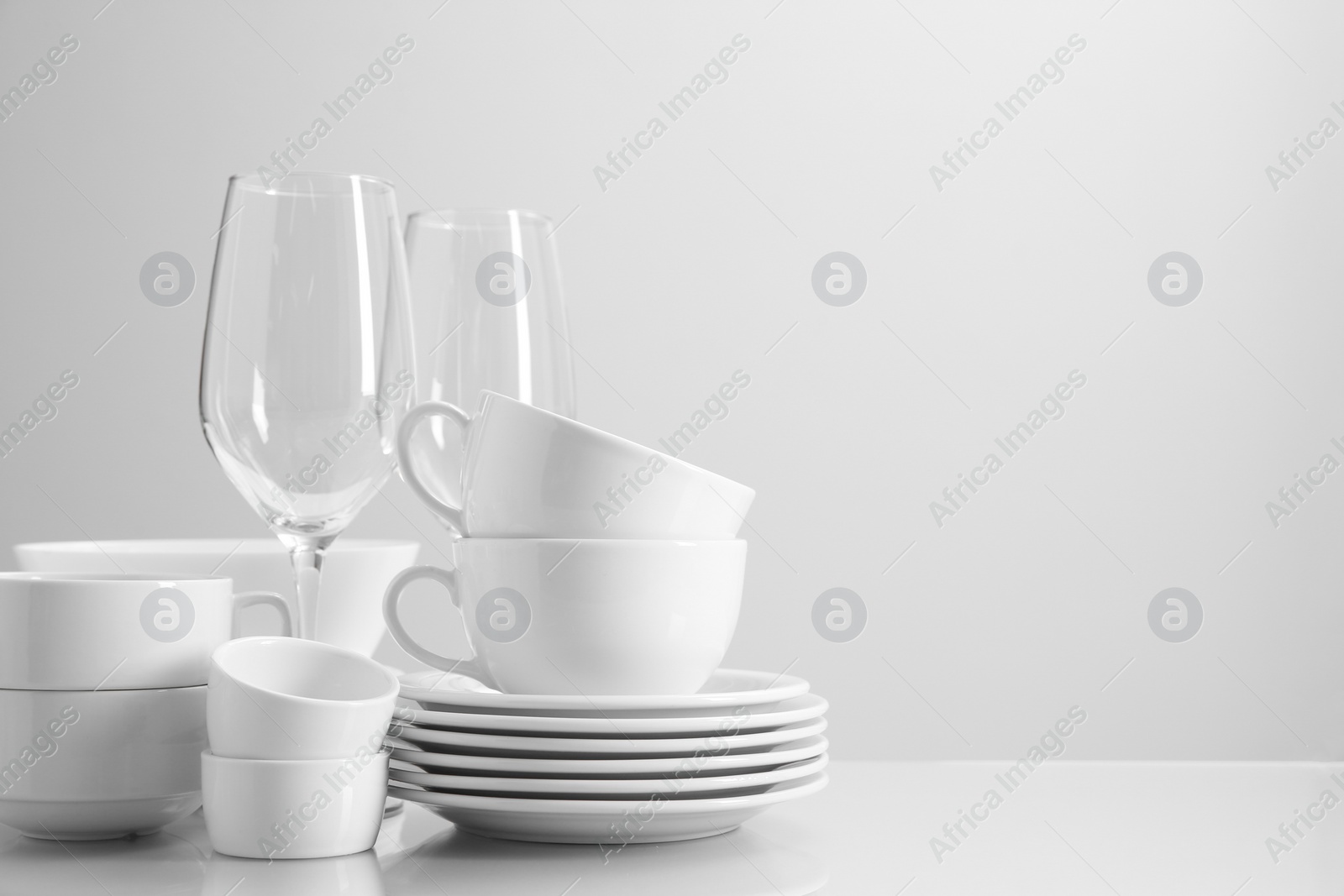 Photo of Set of many clean dishware and glasses on light table. Space for text