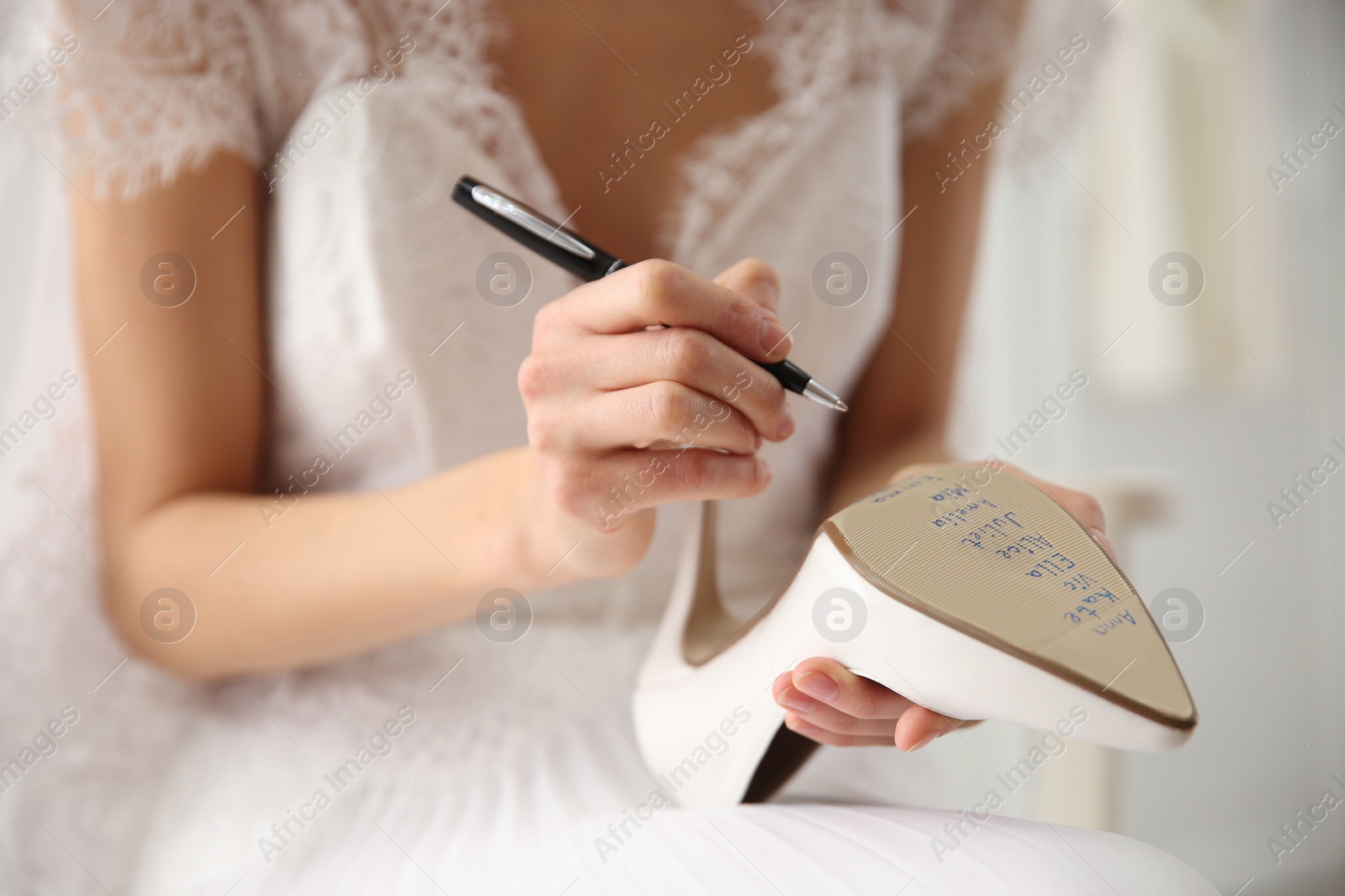 Photo of Young bride writing her single friends names on shoe indoors, closeup. Wedding superstition