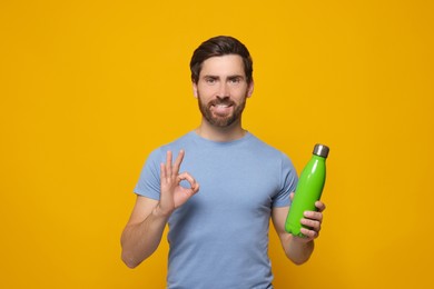 Man with green thermo bottle showing ok gesture on orange background. Space for text