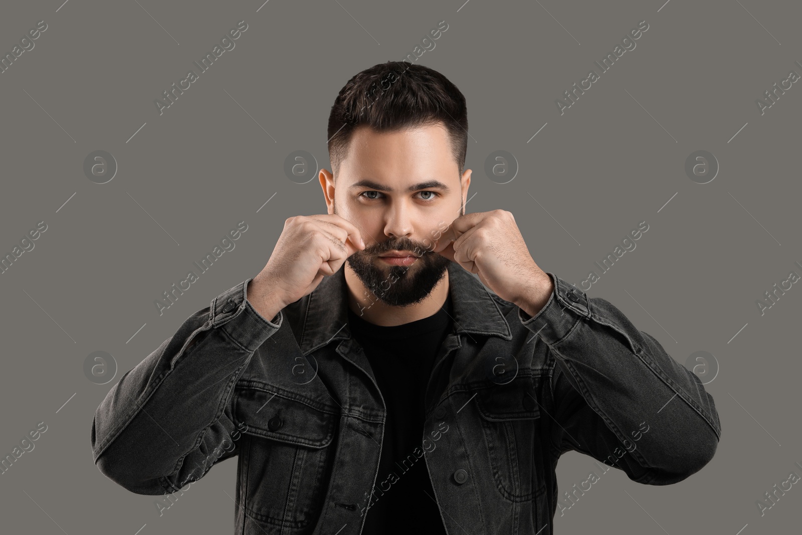 Photo of Young man touching mustache on grey background