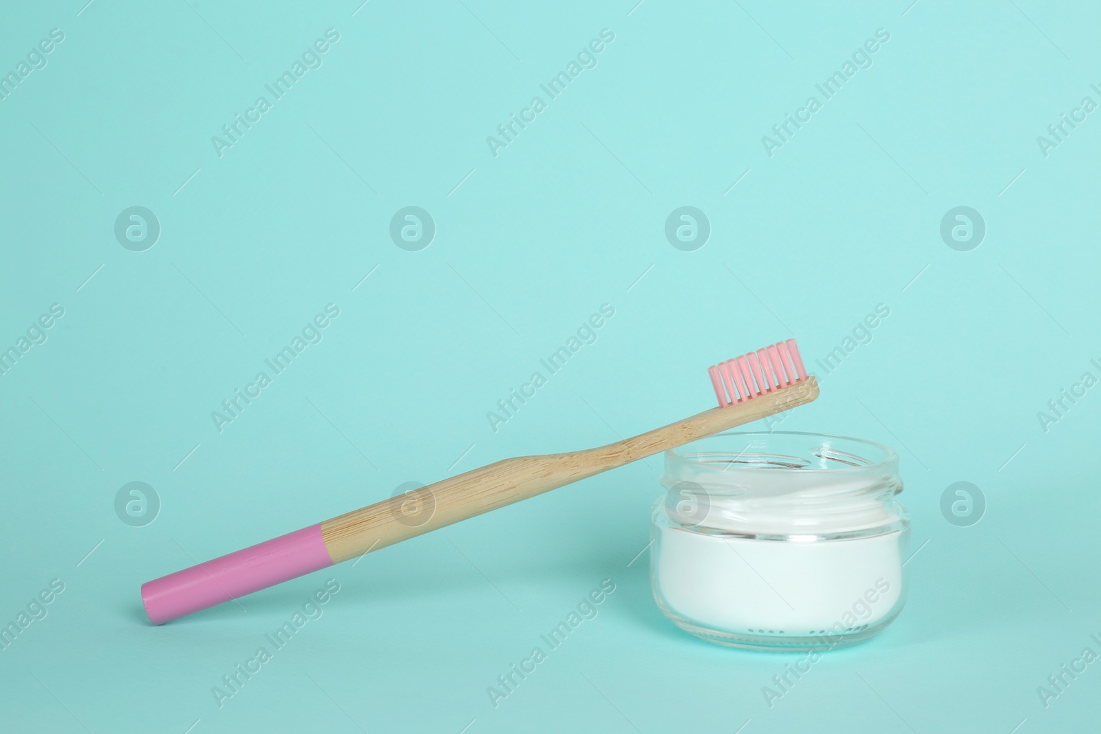 Photo of Bamboo toothbrush and bowl with baking soda on turquoise background