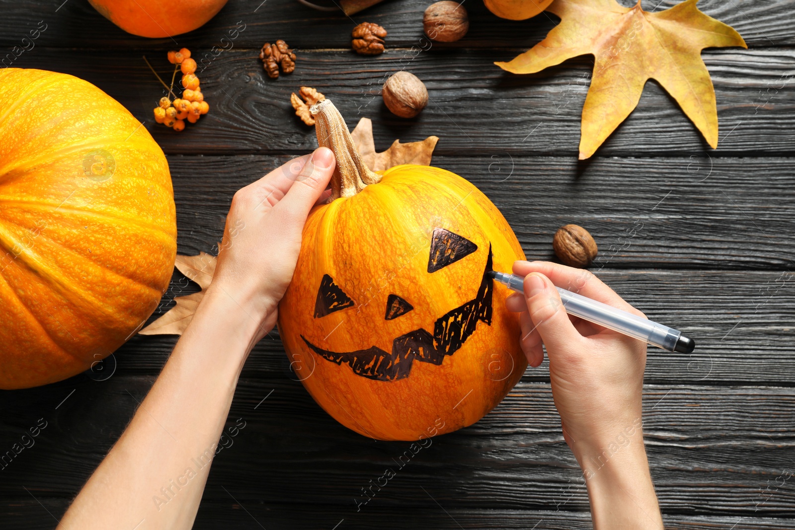 Photo of Woman making Halloween pumpkin head jack lantern on wooden table, closeup