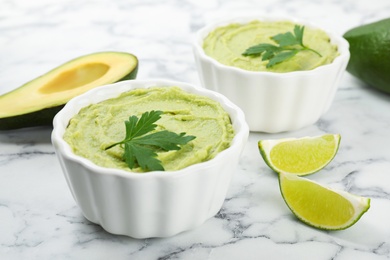 Bowls of guacamole with cut avocado and lime on marble table