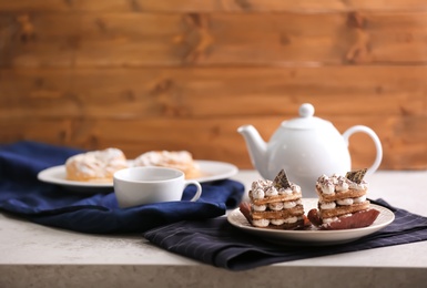 Plate with tasty pastries, teapot and cup on table