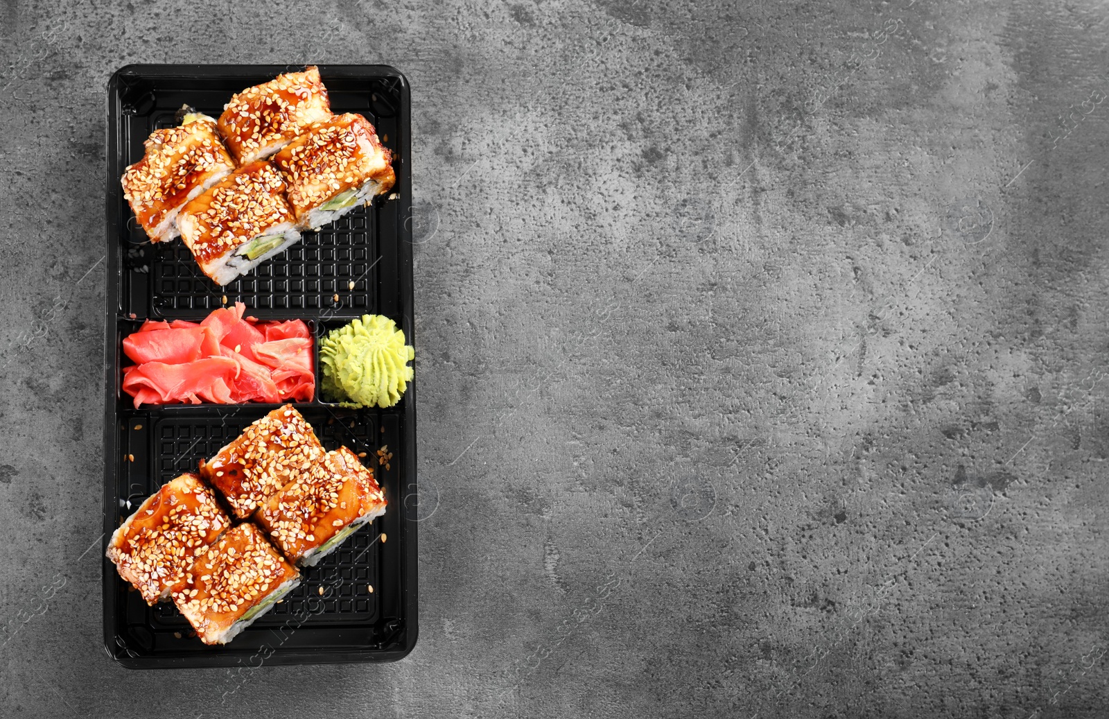 Photo of Tasty sushi rolls in box on grey table, top view with space for text. Food delivery