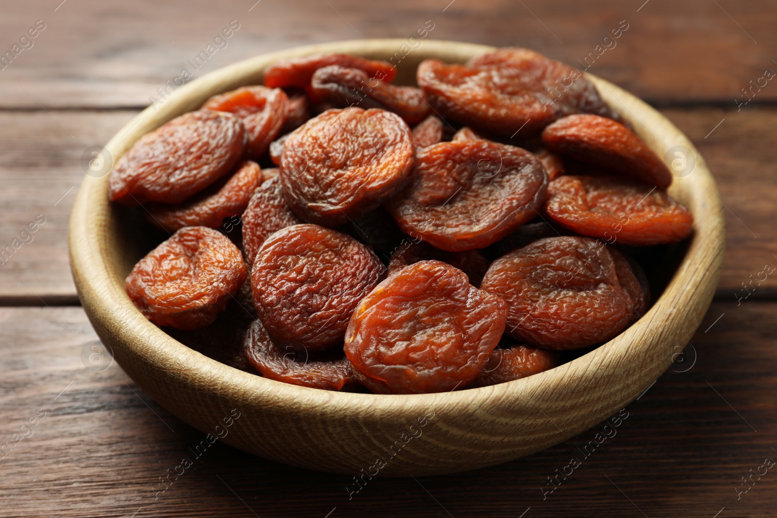 Photo of Bowl of tasty apricots on wooden table, closeup. Dried fruits