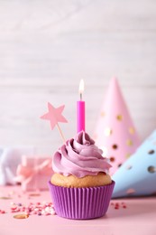 Photo of Birthday cupcake with burning candle, party hats and gift boxes on pink table