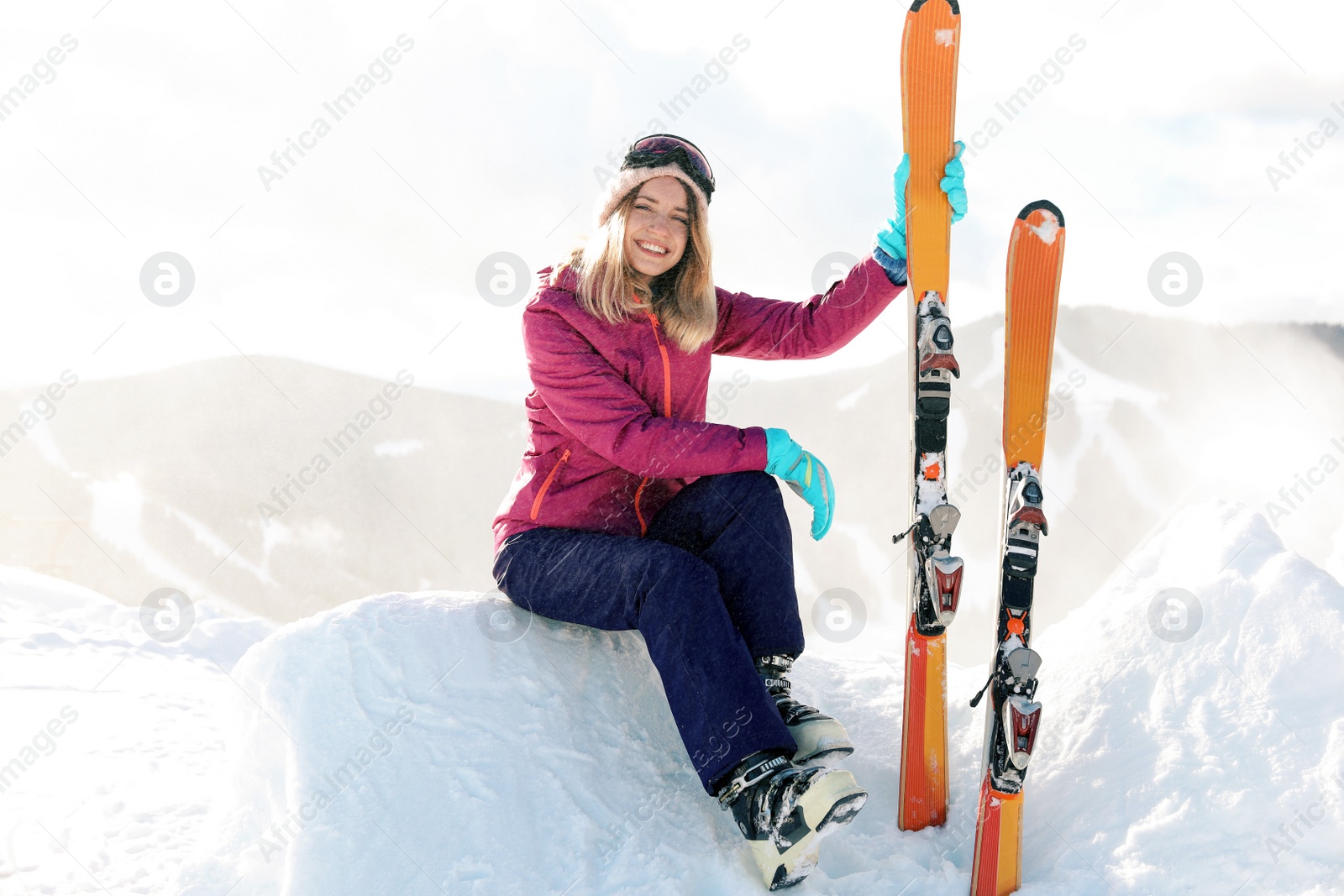 Photo of Young woman with ski equipment sitting on snowdrift in mountains. Winter vacation