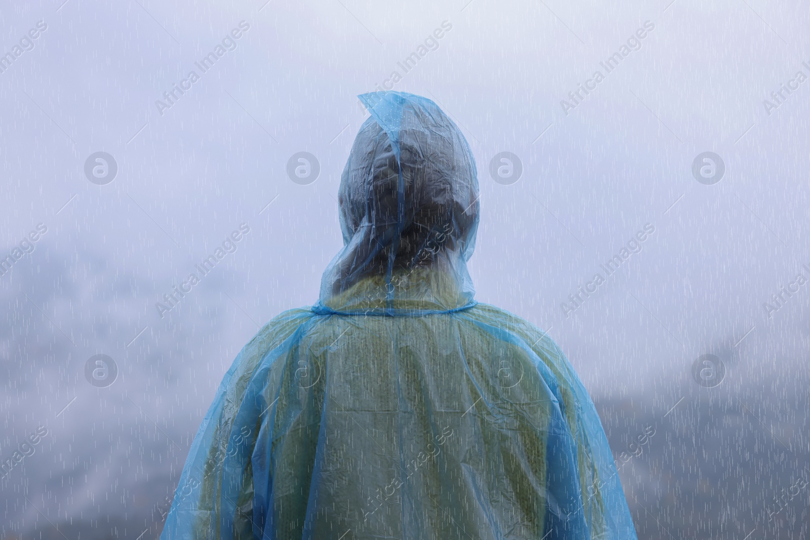 Photo of Woman in raincoat enjoying mountain landscape under rain, back view