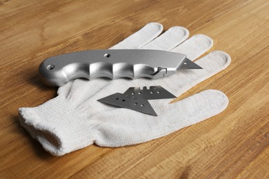Photo of Utility knife, blades and glove on wooden table
