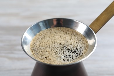 Photo of Turkish coffee pot with hot drink on white wooden table, closeup