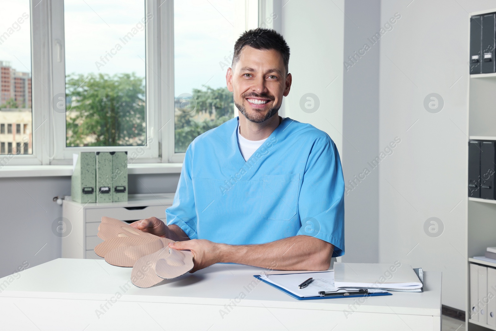 Photo of Handsome male orthopedist showing insoles in hospital