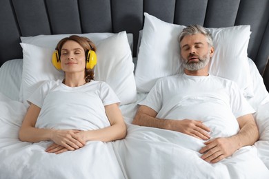 Photo of Smiling woman with headphones lying near her snoring husband in bed at home