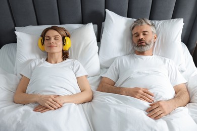 Smiling woman with headphones lying near her snoring husband in bed at home