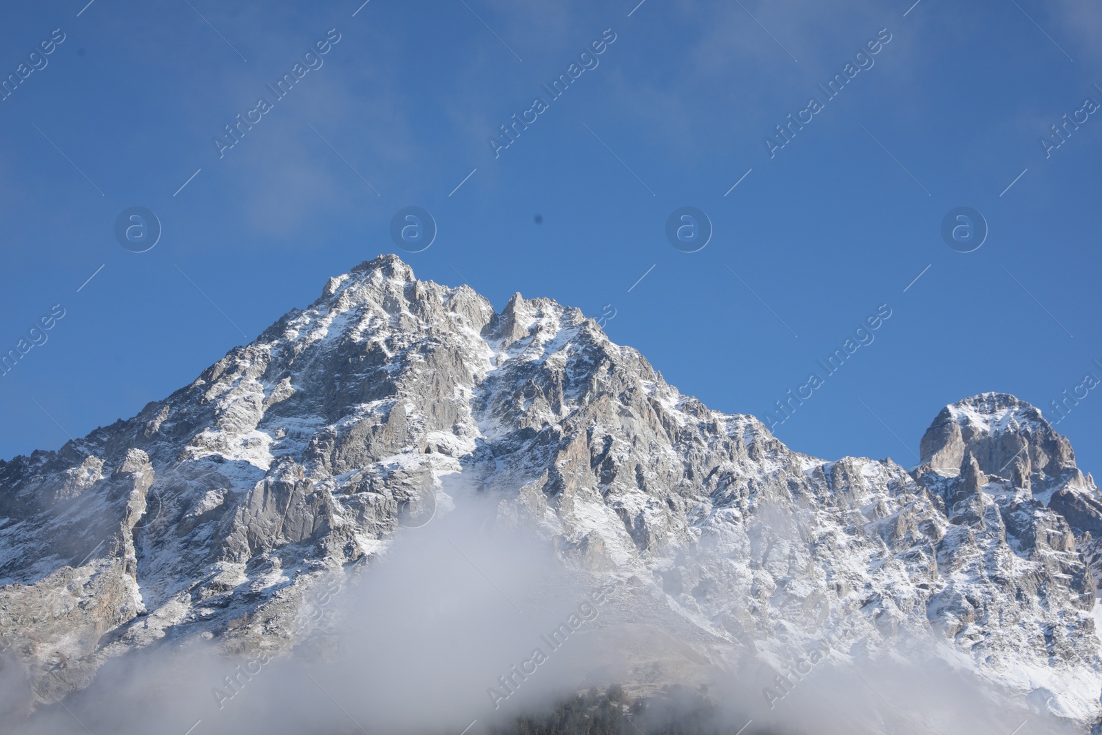 Photo of Picturesque landscape of high mountains covered with thick mist under blue sky