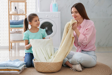 Mother and little daughter with clean laundry in bathroom