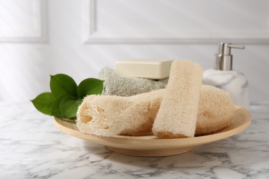 Photo of Loofah sponges, soap, towel and green leaves on white marble table