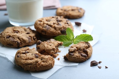 Photo of Tasty chocolate chip cookies and mint leaves on light grey table, closeup