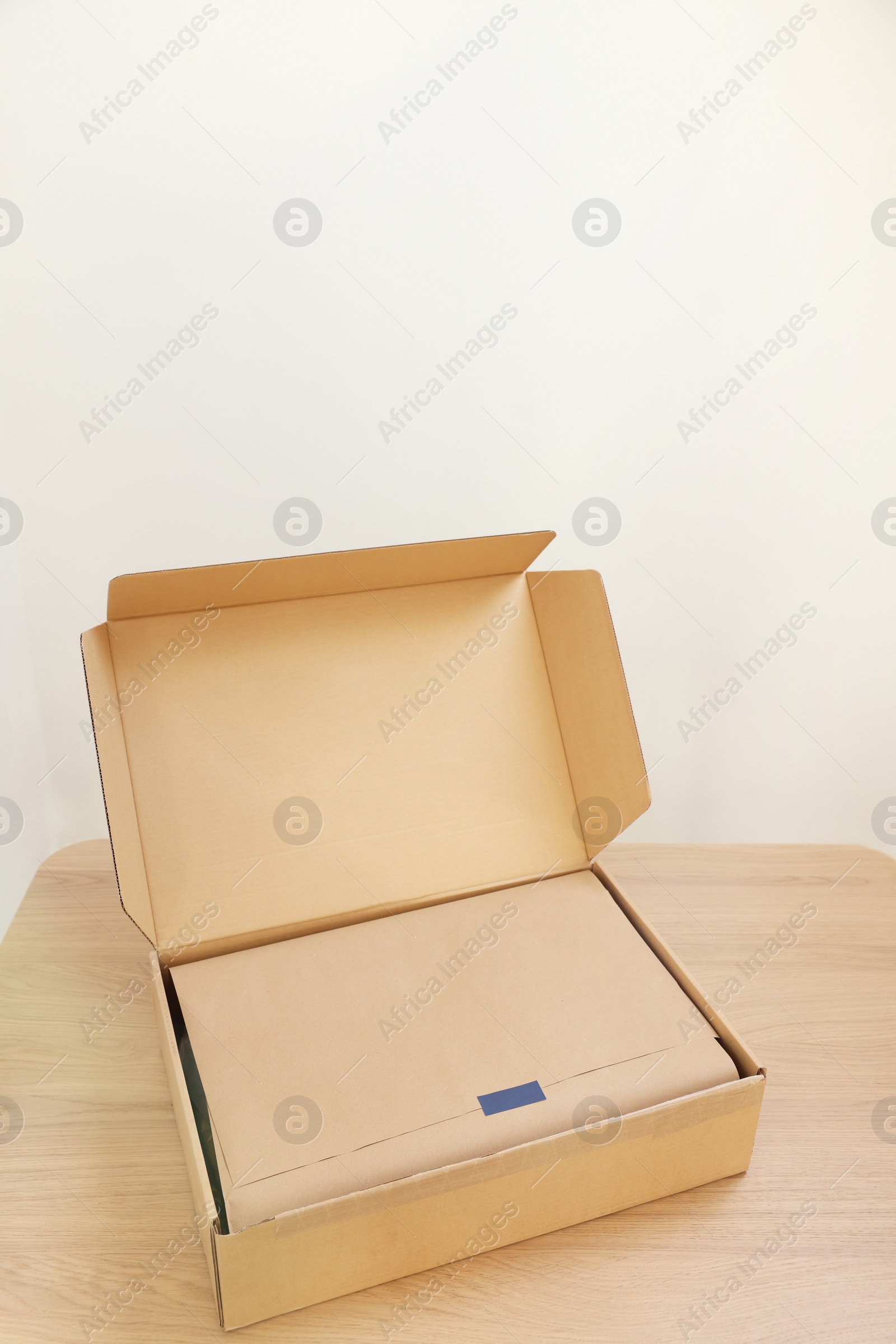 Photo of Open cardboard box with item wrapped in kraft paper on wooden table. Delivery service