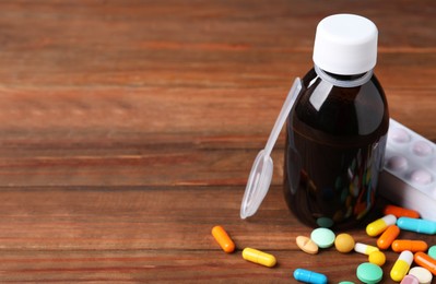 Bottle of syrup, dosing spoon and pills on wooden table, space for text. Cold medicine