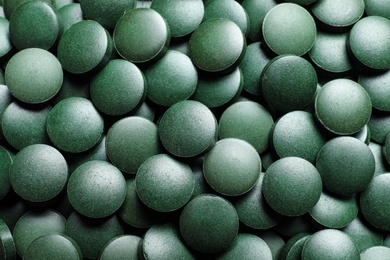 Photo of Green spirulina pills as background, closeup view