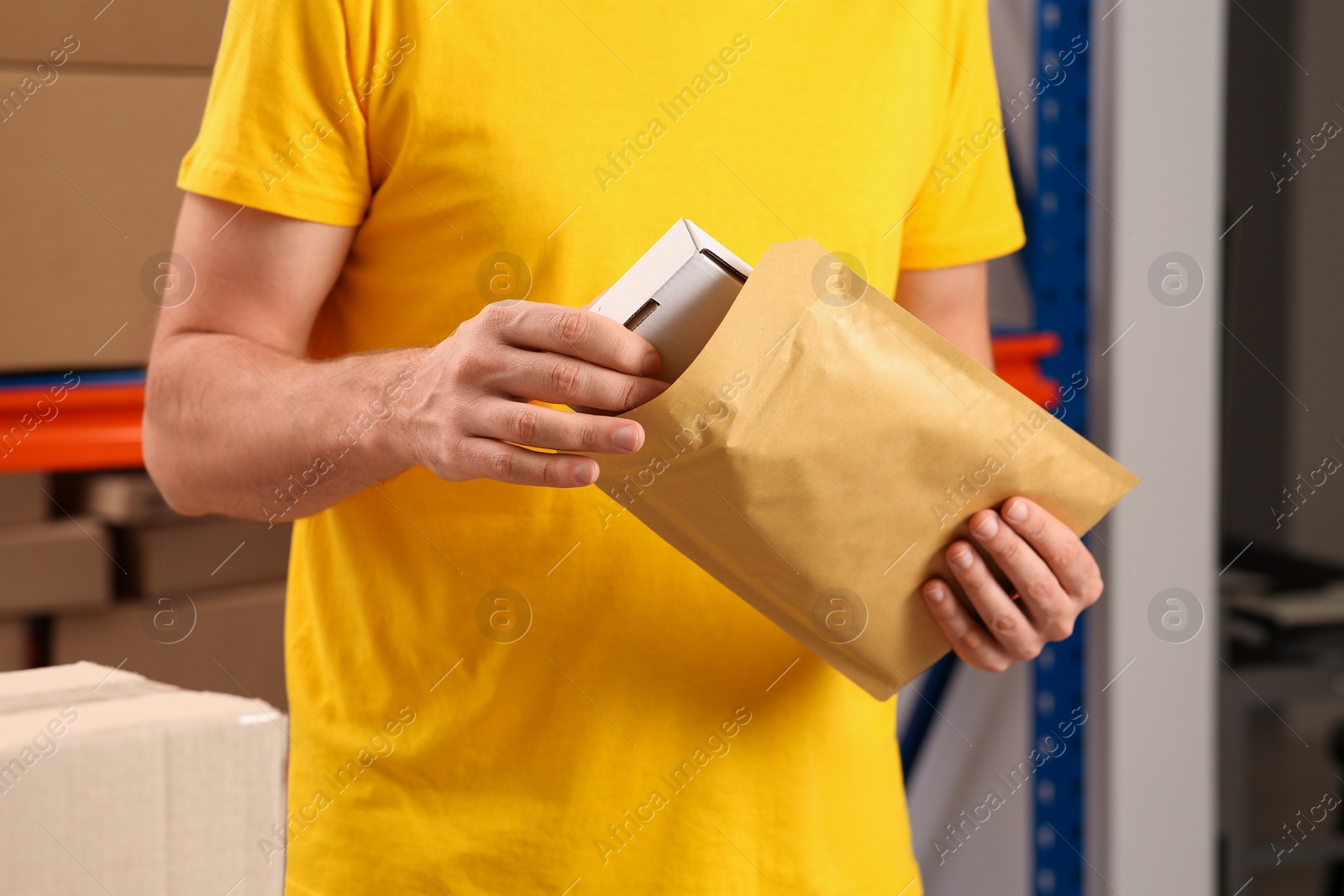 Photo of Post office worker putting box into adhesive paper bag indoors, closeup