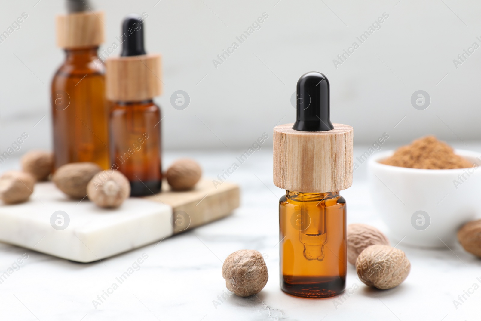 Photo of Bottles of nutmeg oil and nuts on white marble table, closeup. Space for text