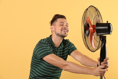 Man refreshing from heat in front of fan on color background