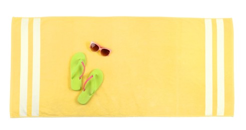 Photo of Yellow beach towel with flip flops and sunglasses on white background, top view
