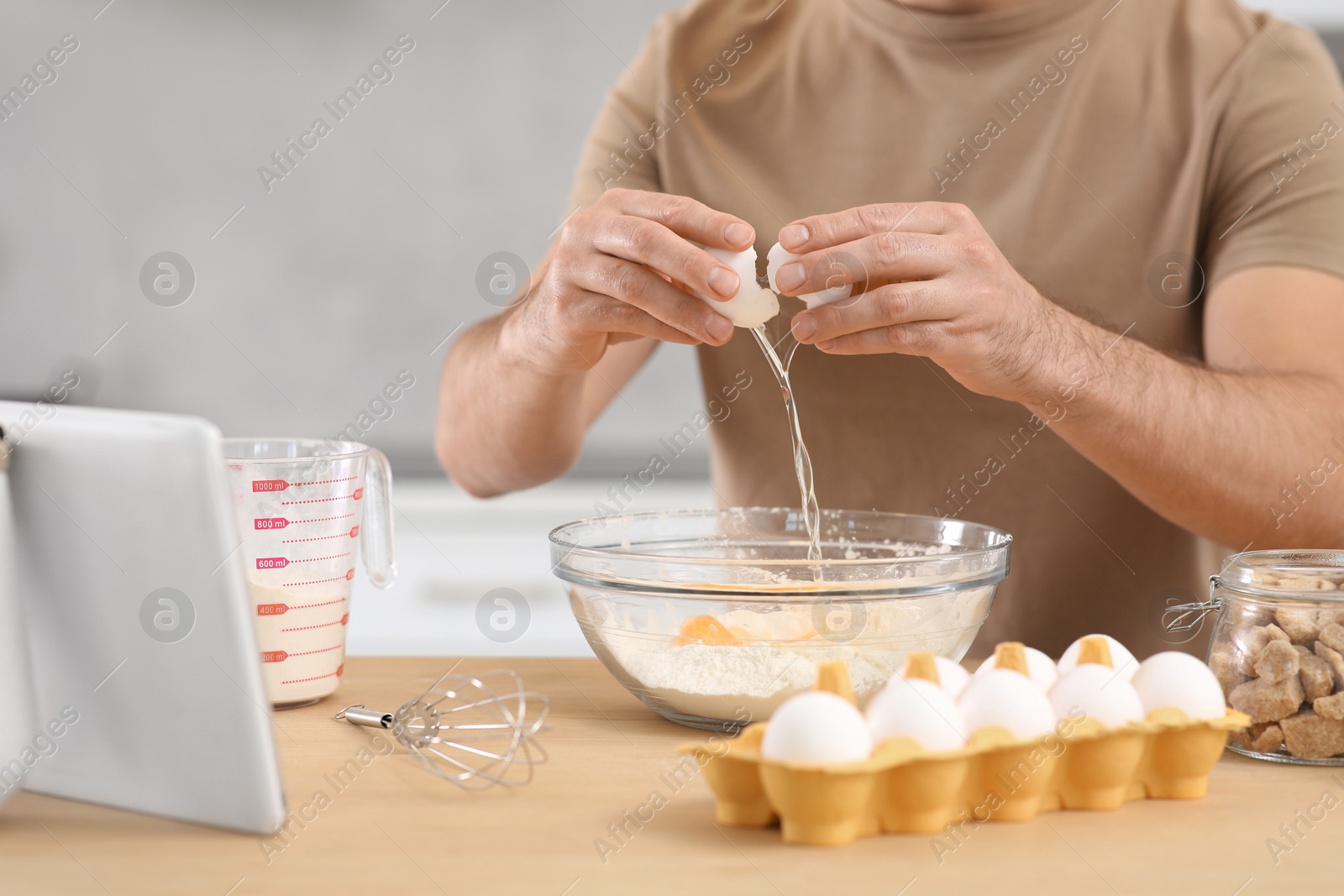 Photo of Man making dough while watching online cooking course via tablet in kitchen, closeup